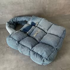 an odd shaped seat cushion made out of jeans on the floor in front of a concrete wall