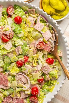 a salad with ham, tomatoes and lettuce in a white dish on a wooden table