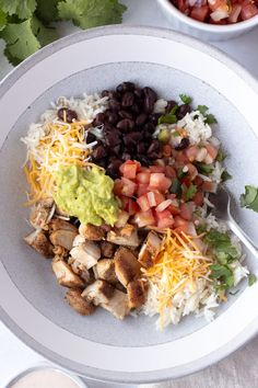 a white bowl filled with rice, black beans and guacamole next to a cup of salsa