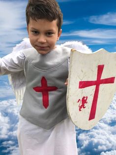 a young boy dressed in an angel costume holding a shield and cross on it's chest