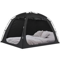 a black tent with white sheets and pillows on the inside is open to show an unmade bed