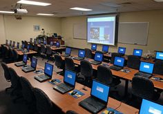 rows of laptops are lined up in front of a projector screen