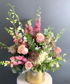 a gold vase with pink and white flowers on a table next to a gray wall