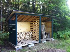 there is a shed made out of wood in the woods with firewood stacked inside