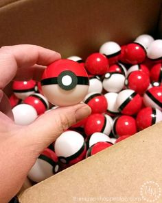 a hand is holding a pokeball in a box full of red and white balls