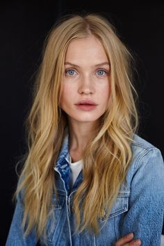 a woman with long blonde hair and blue eyes wearing a denim jacket looking at the camera