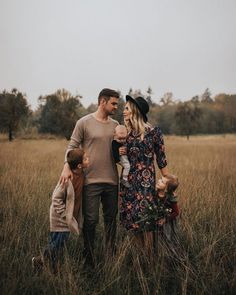 a man, woman and two children are standing in the middle of a field with tall grass