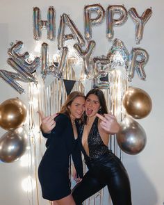 two women pose for a photo in front of balloons and streamers that say happy new year