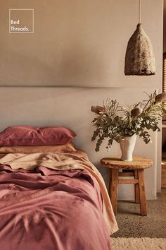 a bed sitting next to a table with a plant on it and a lamp hanging over it