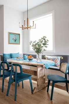 a dining room table with blue chairs and a bench in front of the window that has a potted plant on it