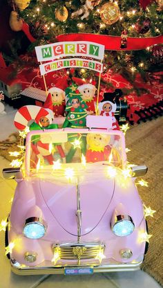 a pink car is decorated with christmas lights and stuffed animals in the back, under a christmas tree