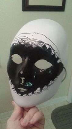 a person holding up a white mask with black hair