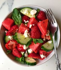 a bowl filled with watermelon cucumber and mint leaves next to a fork