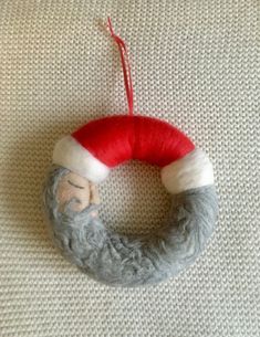 a grey and white knitted wreath with a santa clause on it hanging from a red string