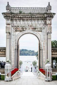 an outdoor wedding ceremony setup with flowers and lanterns on the walkway leading to the water