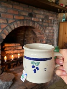 a person holding a coffee mug in front of a fire place