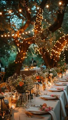 a long table is set with place settings and lights strung from the trees in the background