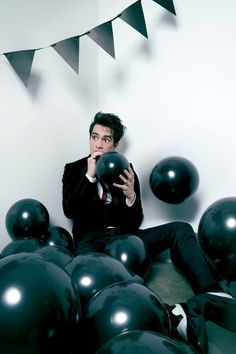 a man sitting on the floor surrounded by black balloons and bunting flags, holding his face to his mouth