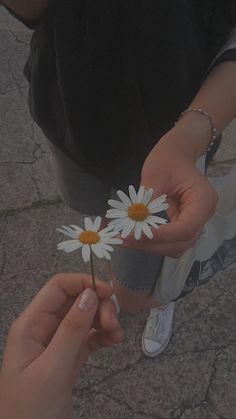 two people holding flowers in their hands on the ground with one person's hand