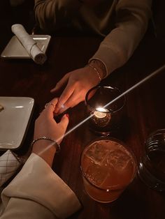 two people sitting at a table with drinks and napkins in front of them, one holding the other's hand