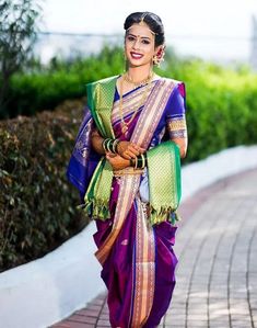 a woman in a purple and green sari is walking down the street with her hands on her hips