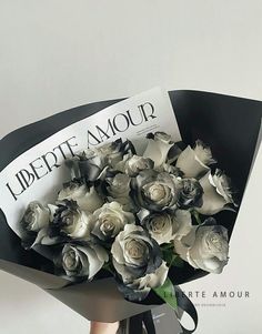 a bouquet of white and black roses is held by a woman's hand with a magazine in the background