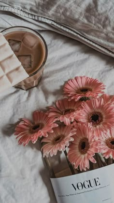 pink flowers on a bed next to a magazine and cup of ice cream with a spoon