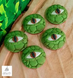 four cookies with green icing decorated to look like an eye and snake's head