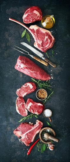 raw steaks with spices and seasonings laid out on a black background, top view