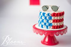 a red, white and blue cake with sunglasses on top is sitting on a stand