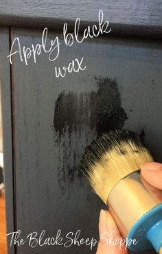 a person holding a paint brush in front of a chalkboard with the words apply black wax on it