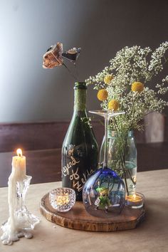 a table topped with vases filled with flowers next to a candle and glass bottle