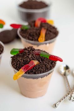 three cups filled with dirt and gummy bears on top of a table next to spoons