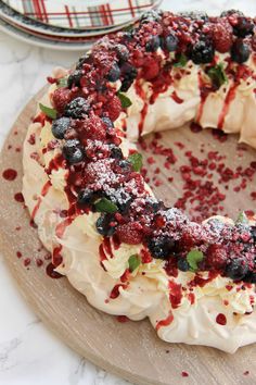 a cake with white frosting and berries on it sitting on a wooden platter