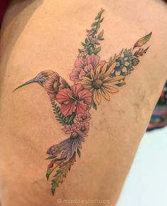 a hummingbird with flowers on its back is shown in this tattoo artist's photo