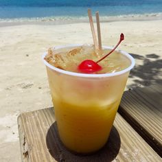 a drink sitting on top of a wooden table next to the ocean with a cherry in it