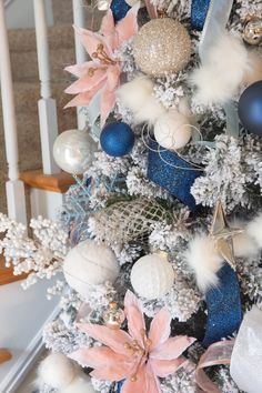 a decorated christmas tree with blue and white ornaments on it's branches, next to stairs