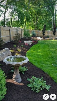 a bird bath sitting in the middle of a lush green yard next to a wooden fence