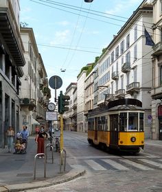 a yellow trolley is going down the street with people sitting on benches in front of it