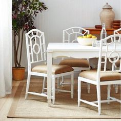 a white table with four chairs and a bowl of fruit on top of the table