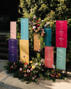 an arrangement of flowers on display in front of a wall with seating cards attached to it