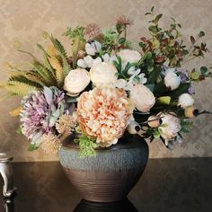 a vase filled with lots of flowers sitting on top of a table next to a wall