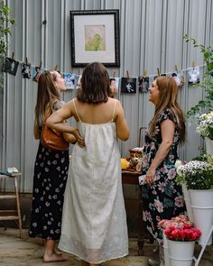 three women standing in front of a table with flowers and pictures hanging on the wall