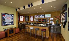 a sports themed home bar with stools and pictures on the wall above it, along with framed baseball memorabilia