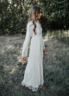 a woman in a white dress is walking through the grass with her hand on her hip