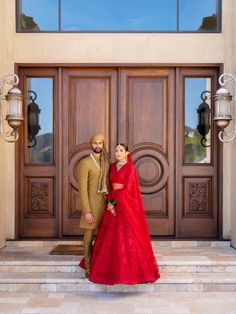 a man and woman standing in front of a large wooden door wearing red dresses, posing for the camera