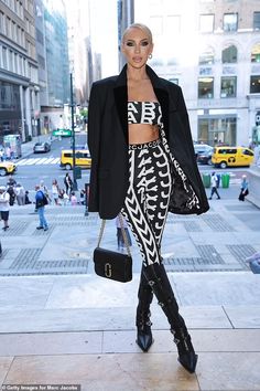 a woman in black and white outfit walking down the street with her hand on her hip