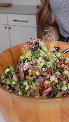 a salad in a wooden bowl on top of a table with a woman looking at it