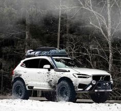 a white suv with skis on top driving through the snow in front of trees