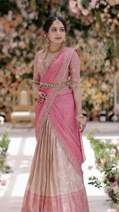 a woman in a pink and beige sari with gold jewelry on her neck, standing outside